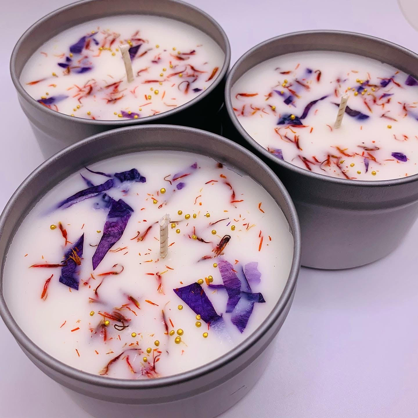 Three white candles in tins with floral inclusions 