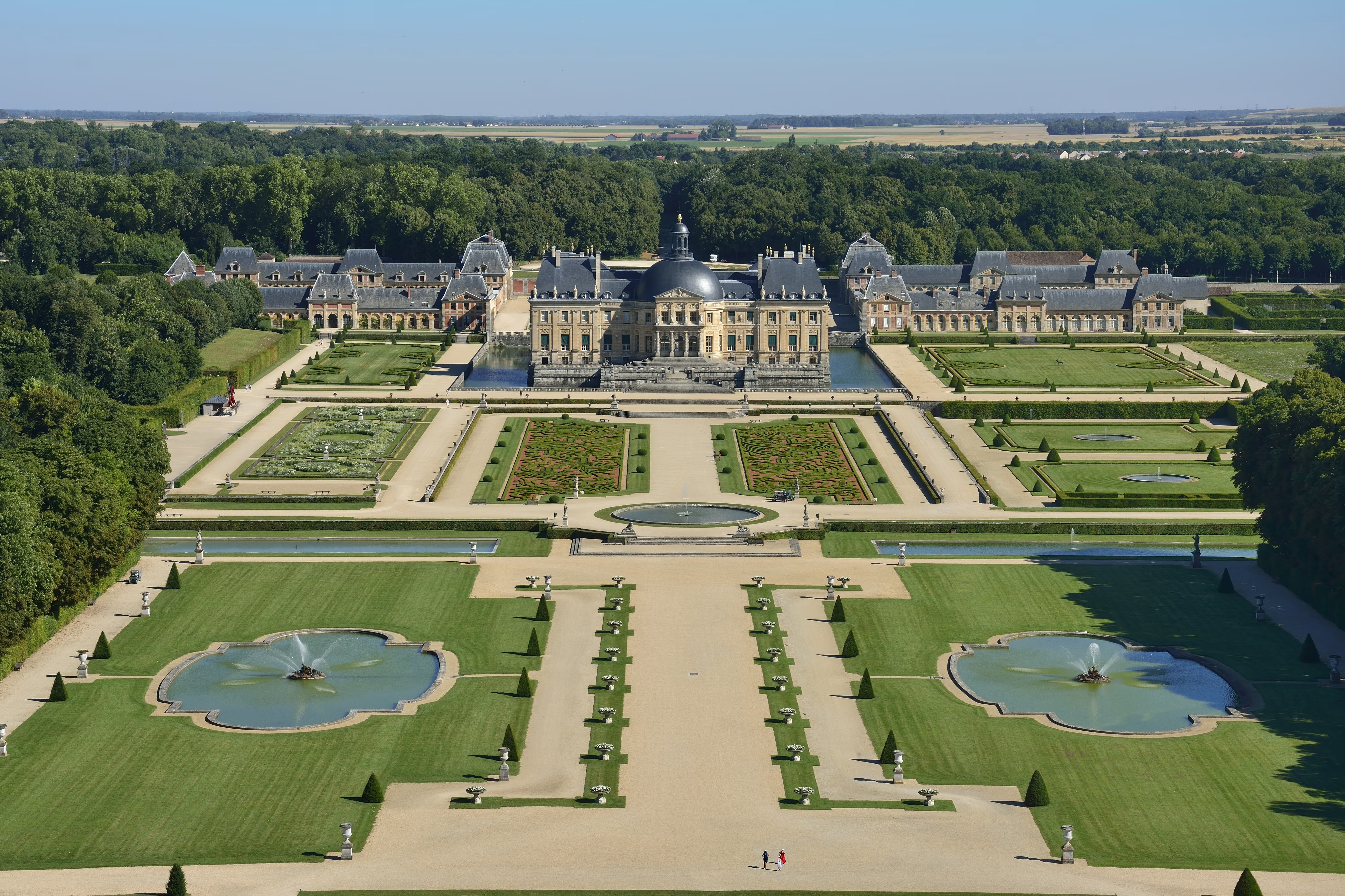 The grand Château de Vaux-le-Vicomte stands surrounded by expansive formal gardens with symmetrical pathways, reflecting pools, and manicured hedges, showcasing the historic elegance and cultural heritage of Seine-et-Marne.