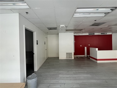The inside of the rental space, with an open door leading to another room on the left. In the back, there is a red painted wall and a counter in front of the wall. There is a closed door in the back on the left-hand side.