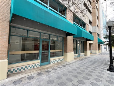 The outdoor entrance of the rental space, showing the view from the sidewalk with a lamp post in front of the building. The rental space has a blue awning providing shade over the entrance and has a blue door.