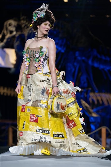 Stephanie Blunt modeling a gown made by Kayla Rieves. The model stands on a runway, dressed in a yellow gown made from farm feed bags.
