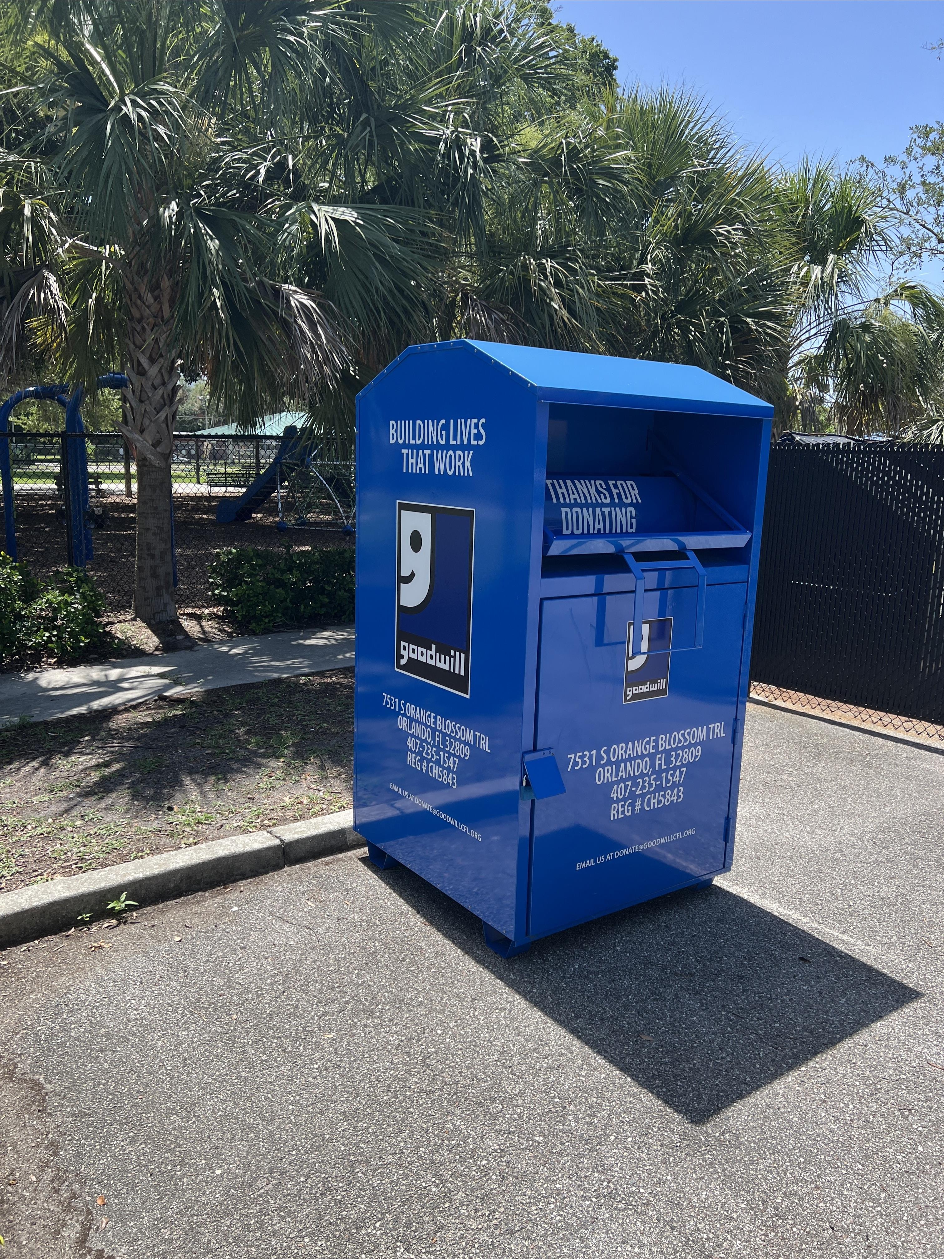 A blue Goodwill donation bin in front of trees located at a neighborhood center