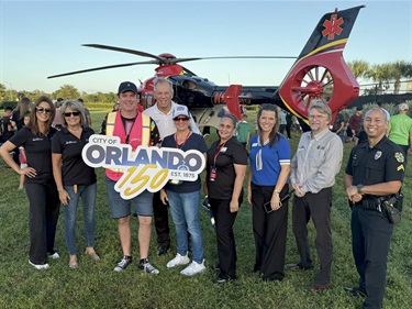 A group of people standing together one of them is holding a sign that says city of orlando 150 with a helicopter in the background 
