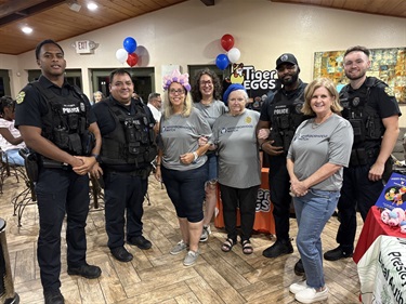 A group of police officers standing with a group of people wearing neighborhood watch shirts with balloons in the background 
