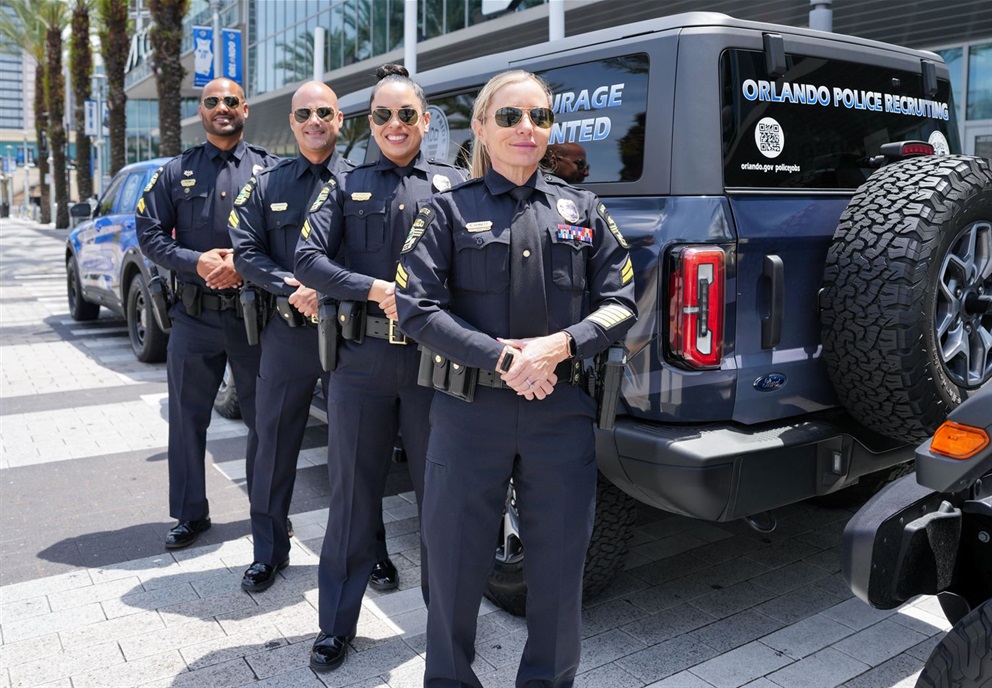 Officers with the Orlando Police Department Recruiting Team stand posed in front of their branded vehicles.