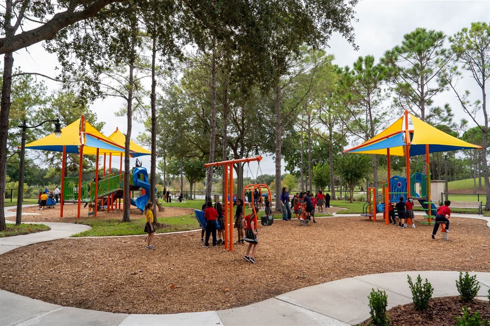 A newly renovated playground at Southport Park Playground featuring yellow, blue, and orange climbing structures, an expanded play zone with a mommy and me swing, single swings and a spiral slide. Children are playing with the brand new equipment.