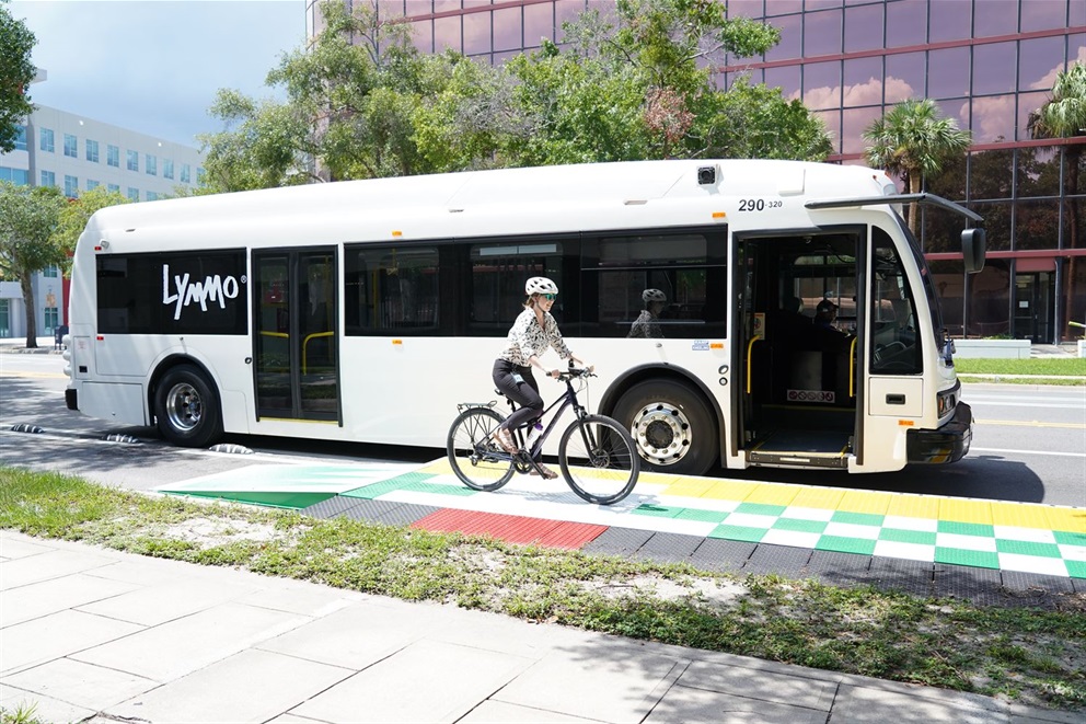 A white Lynmo bus parked in downtown Orlando with a cyclist riding by.