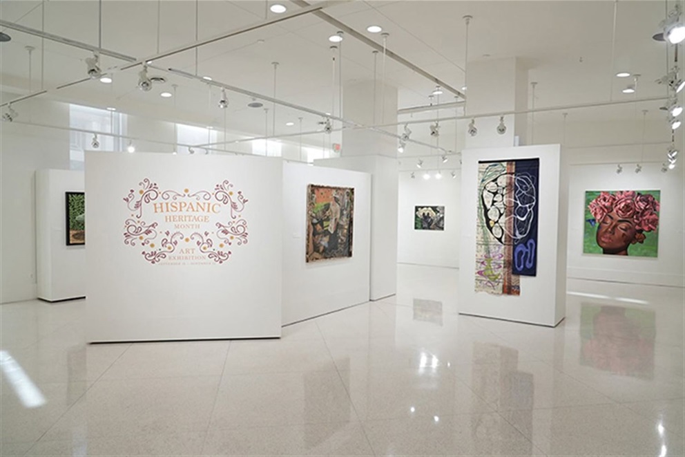 Wide view of the Terrace Gallery at Orlando City Hall showcasing the City of Orlando’s Hispanic Heritage Month Art Exhibition. Colorful original paintings and mixed-media artwork are displayed on white gallery walls throughout a bright, contemporary exhibition space celebrating Hispanic art and culture.
