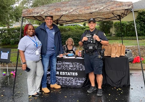 Commissioner Ortiz and an OPD Officer posing next to residents of Dover Estates next to a branded table