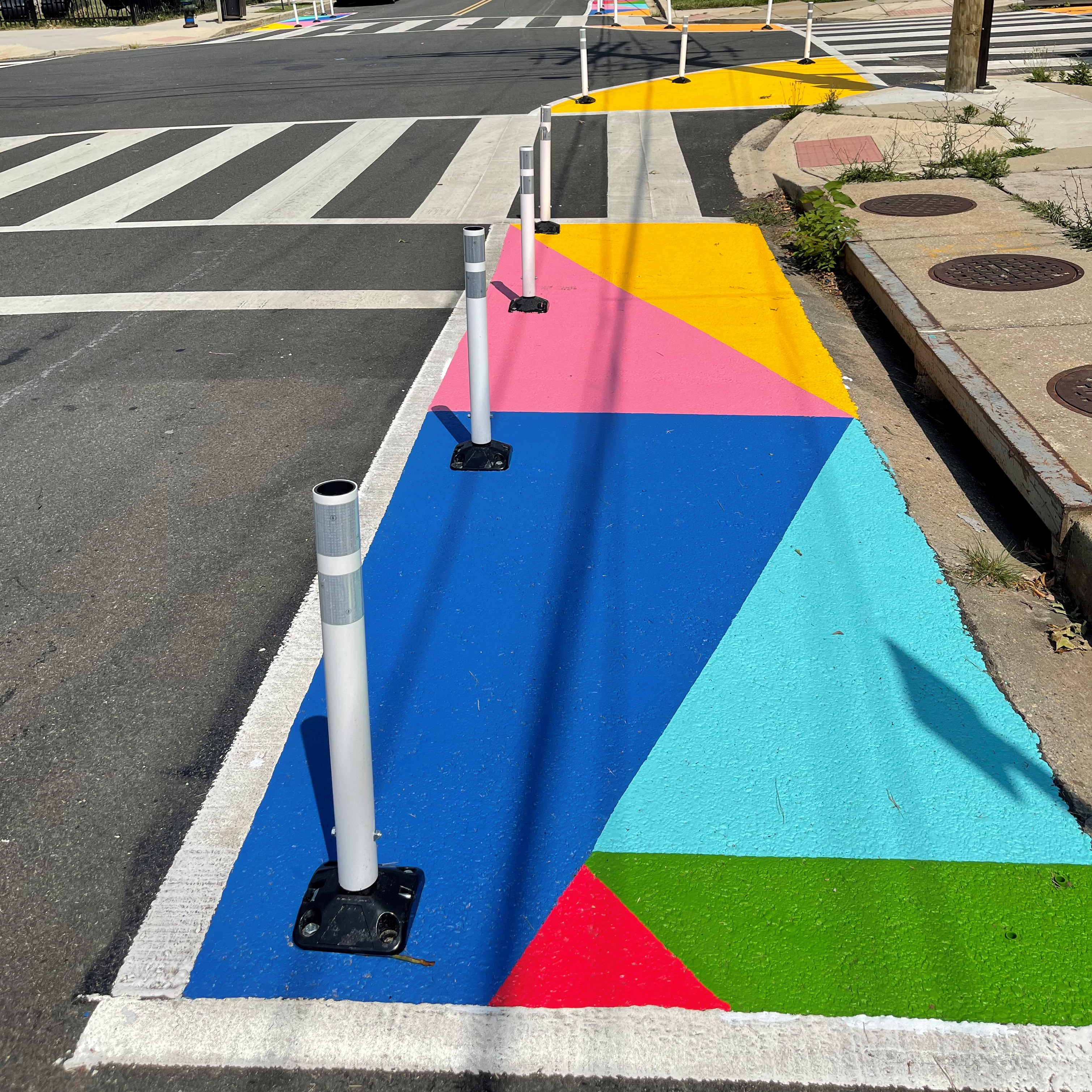 A parking lane near an intersection that has been turned into a curb extension painted with bright colors and bounded with flexible posts