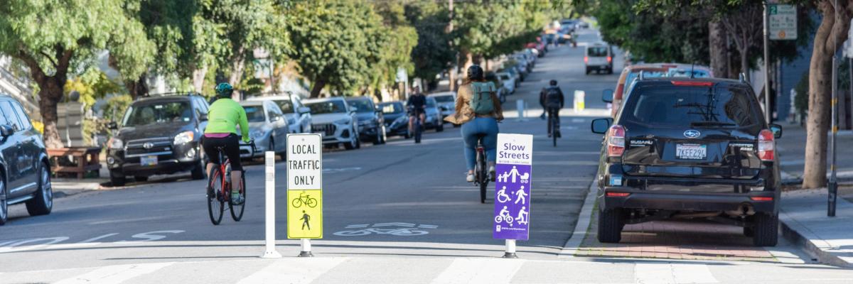 A roadway has signage indicating local traffic only and branding for the SFMTA slow streets program. 