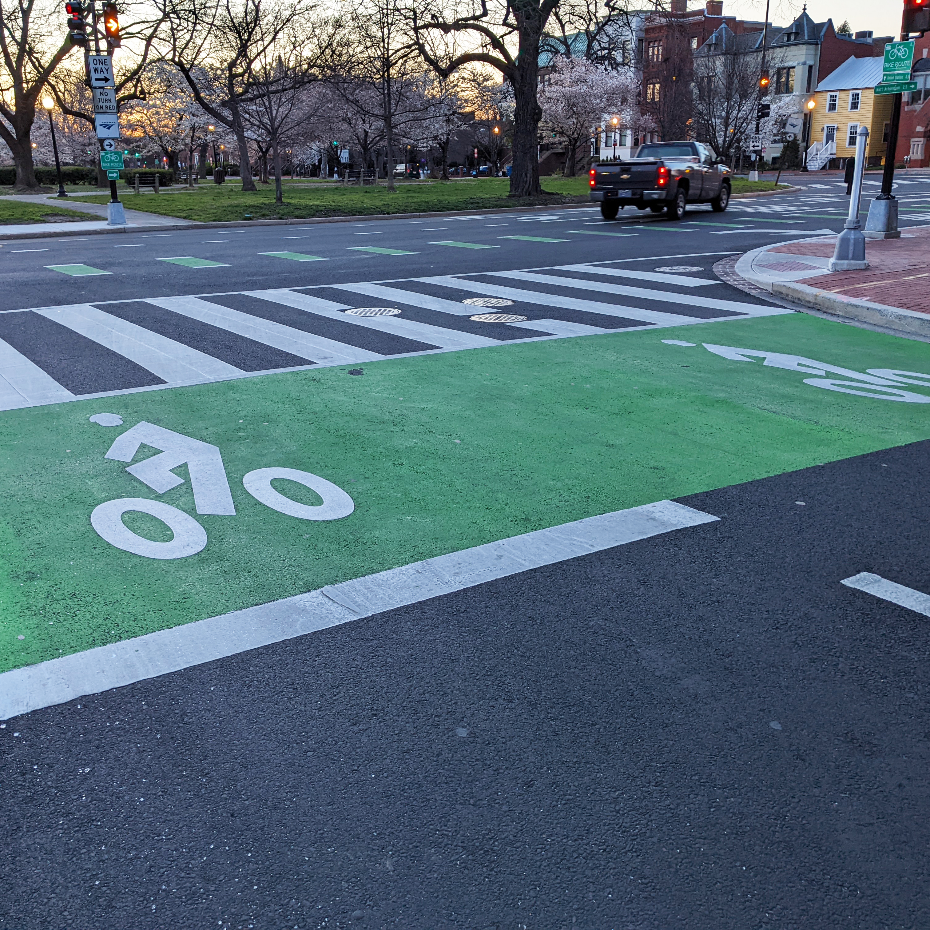 A green box with a sharrow is panted across the roadway, parallel to a crosswalk, providing a space for bikes to wait at the signal ahead of queueing vehicles.