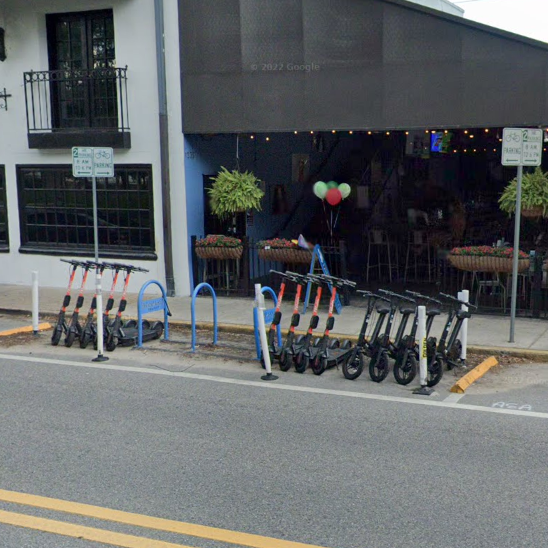 A photo of shared scooters parked within a corral on a street. The corral is located in an on-street parking lane and is demarcated by striping and flexposts.