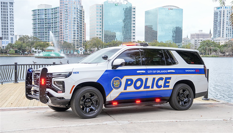 Orlando Police Department Tahoe parked along the Lake Eola waterfront with its lights illuminated. The vehicle is positioned near a railing overlooking the lake, with the fountain and downtown Orlando high-rise buildings visible in the background.