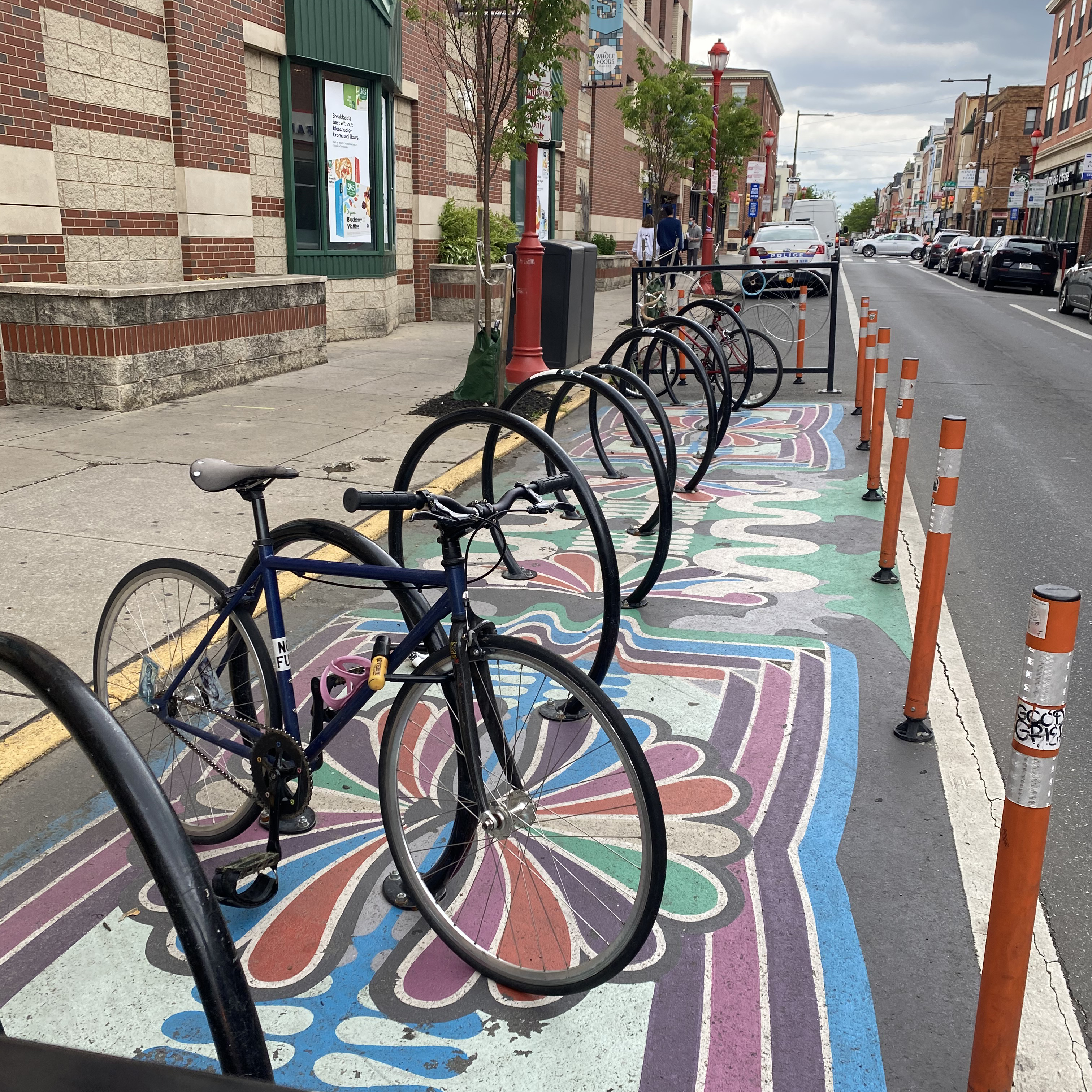 A photo of bicycles parked within a corral on a street. The corral is located in an on-street parking lane and is demarcated by striping and flexposts. A mural is painted within the corral.